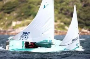A Hansa with a mainsail and jib sailing near a rocky shore